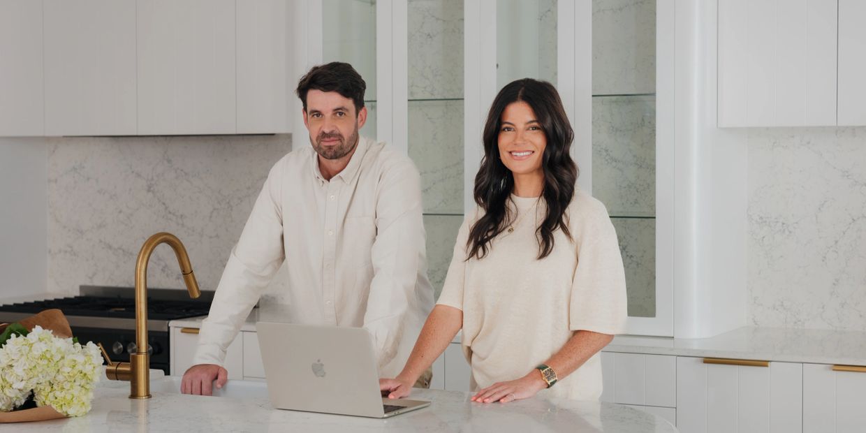 A man and woman standing together in a modern white kitchen with a laptop.