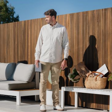 Man in beige pants and white shirt standing outdoors with a phone in hand.