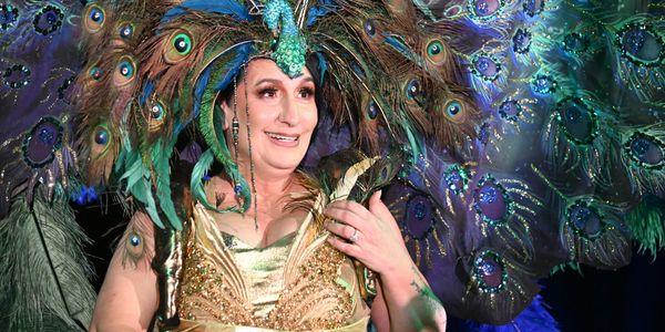 Person in a vibrant peacock costume with feathers and jewels.