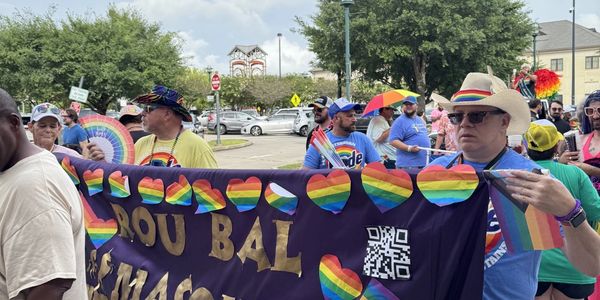 People holding a rainbow-themed banner at a pride parade.