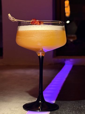 Elegant cocktail with frothy top and garnish, served in a black-stemmed glass.