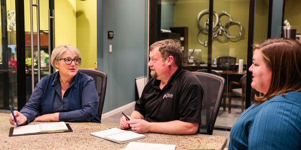 Three colleagues engaged in a meeting around a conference table.