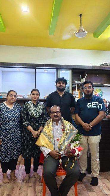 Group photo with a seated man holding flowers, draped in a ceremonial shawl.
