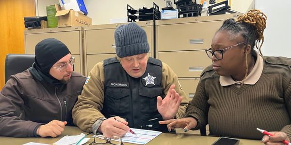 Three people in a discussion, one in police uniform explaining paperwork.