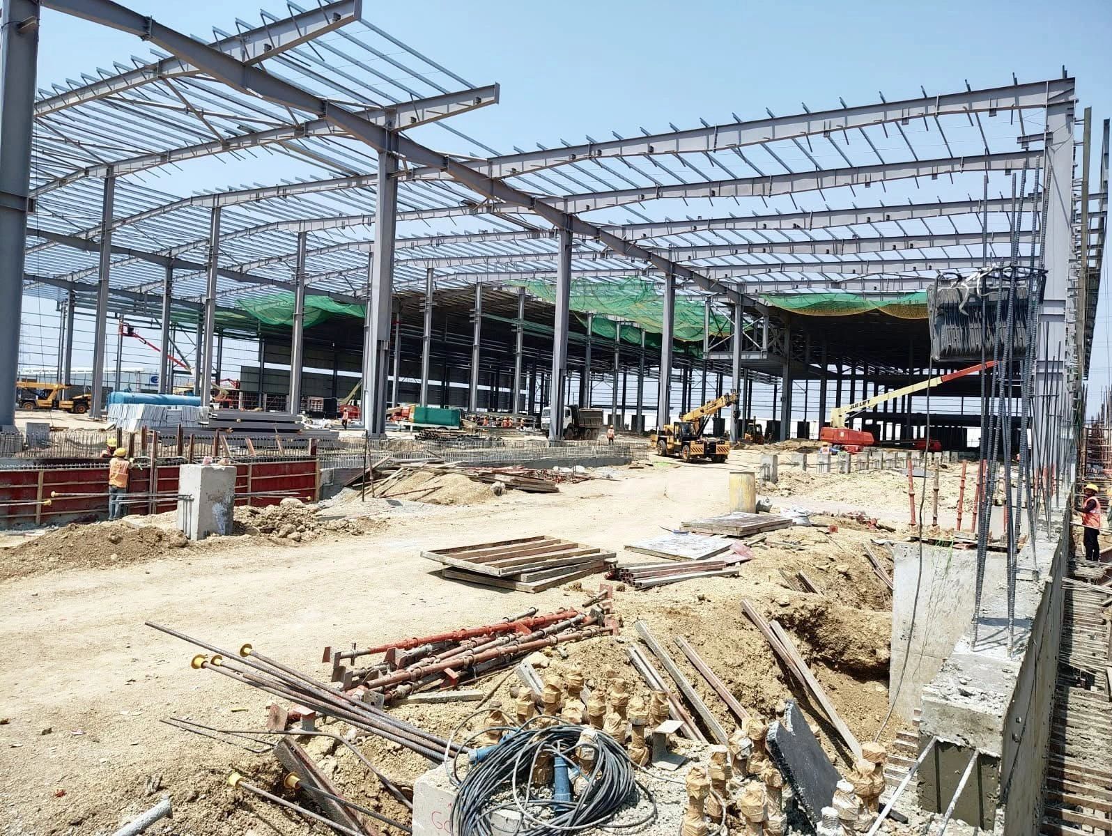Large industrial building under construction with steel framework and construction equipment.