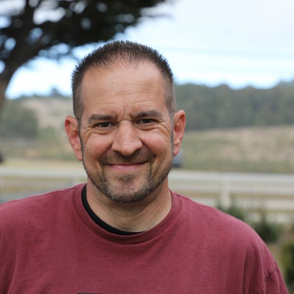 Smiling man outdoors in a maroon shirt.