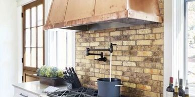 Modern kitchen with copper range hood and brick backsplash.