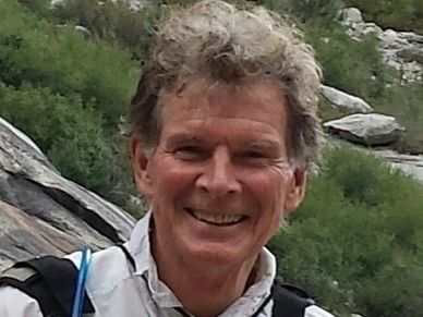 Smiling man outdoors with rocky and green background.