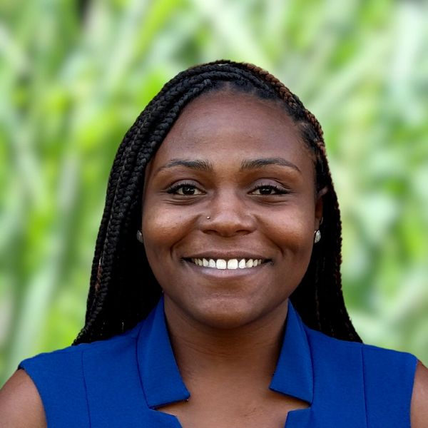 Smiling woman with braided hair in a blue top against a green blurred background.