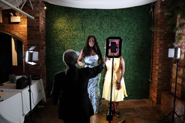 Two woman posing on a 360 photo booth ,with another woman instructing them what to do