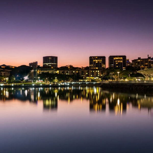 City skyline reflecting on calm water at dusk with vibrant lights.