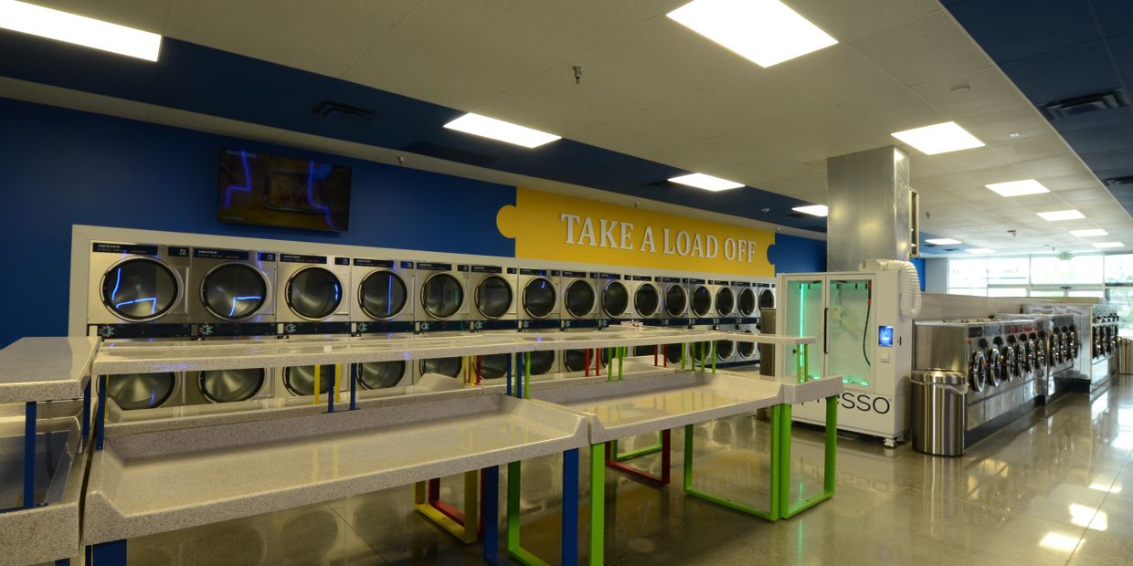 Interior of a bright, modern laundromat with multiple washers and dryers.