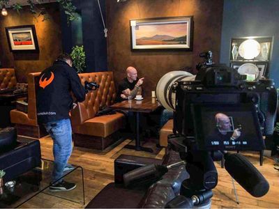 A photographer captures a bald man sitting at a cafe table.