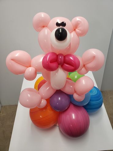 A balloon sculpture of a pink bear with colorful balloons as a base.
