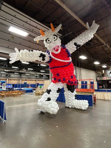 A large cow sculpture made entirely of balloons inside a warehouse.