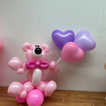 Pink balloon sculpture of a bear holding heart-shaped balloons.