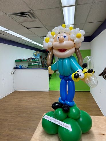 Colorful balloon sculpture of a person holding a bee in a classroom.