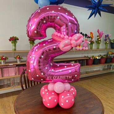 Pink number 72 balloons with polka dots on a table, decorated with flowers.