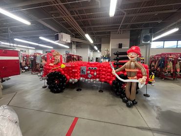 Large balloon sculpture of a red fire truck with firefighter figures inside and outside.