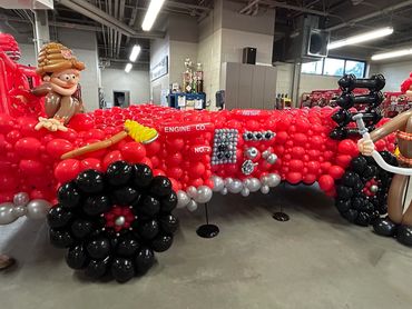 A fire truck made entirely of red, black, and silver balloons with balloon firefighters.