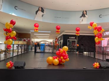 Decorated stage with red and gold balloons in a shopping mall.