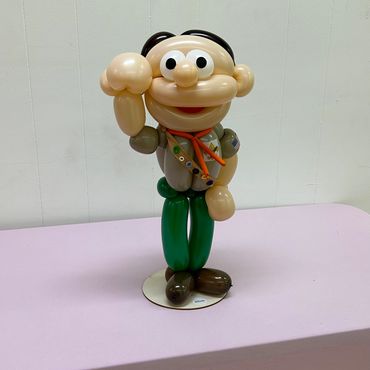 A balloon sculpture of a cartoonish scout character with green pants and a brown shirt.