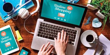 Person shopping online with laptop, tablet, and smartphone on a wooden desk.