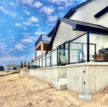 New modern house with a glass railing on a sandy lot.