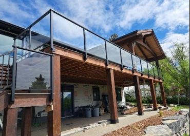 Modern patio deck with glass railing and wooden beams.