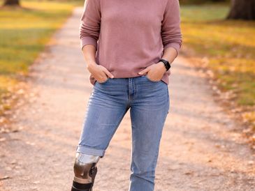 Young woman with a prosthetic leg standing confidently on a park path.