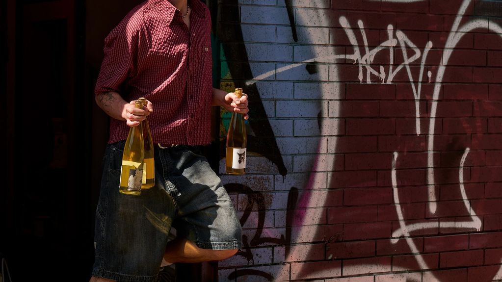 Person holding three bottles of wine against a graffiti wall.