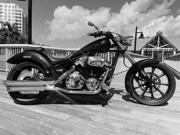 A shiny black motorcycle parked on a wooden deck under a blue sky.