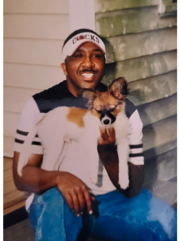 Man in a visor holding a small dog while sitting outside.