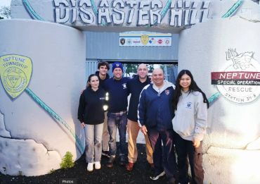Group of six people posing in front of Disaster Hill entrance with rescue logos.