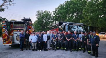 Group photo of firefighters and emergency responders beside fire trucks.
