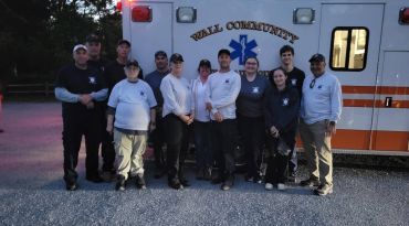 Group of emergency responders posing in front of an ambulance at dusk.
