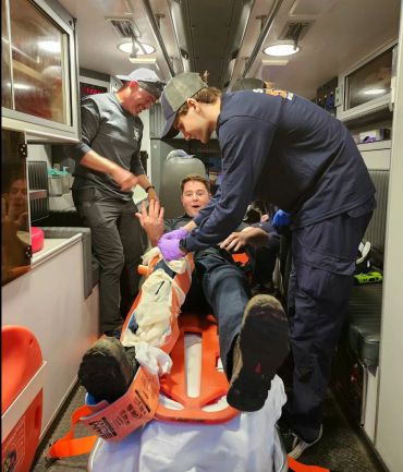 Emergency responders assist a man on a stretcher inside an ambulance.