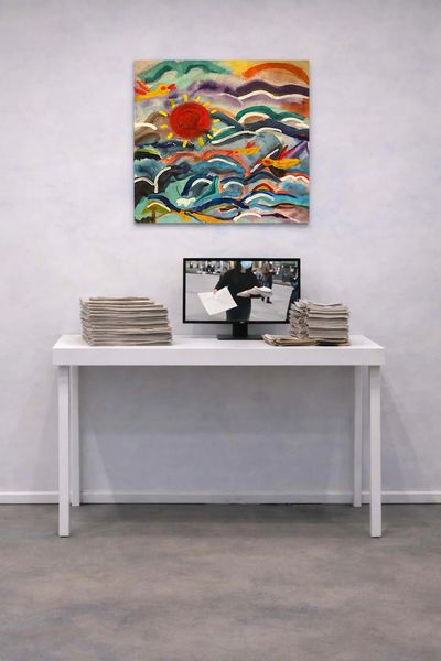 White table with stacks of newspapers and a monitor showing a person distributing papers.