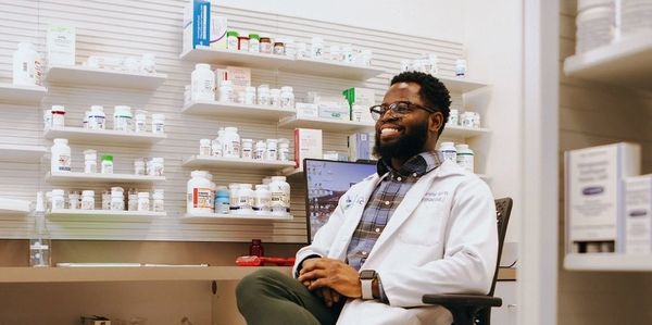 Pharmacist smiling in a pharmacy surrounded by medicine bottles.