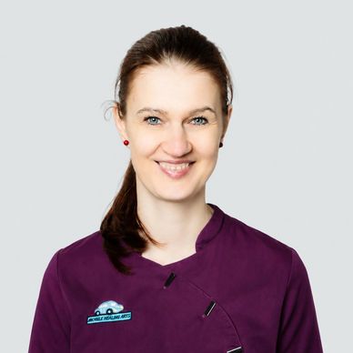 Porträt einer lächelnden Frau mit braunen Haaren in einem violetten Berufskittel.