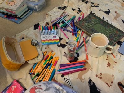 Art supplies, a coffee cup, and a book on a cloth with dog prints.