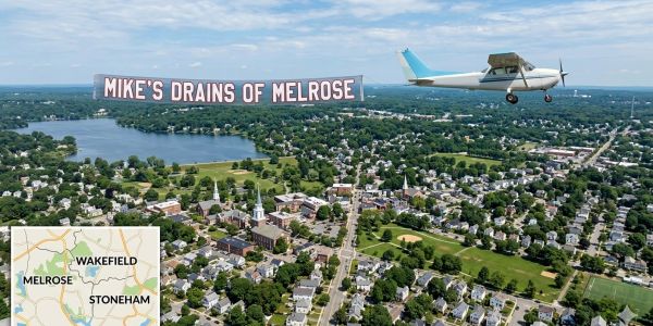 Small plane towing a banner advertising Mike's Drains of Melrose.