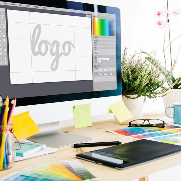A designer's workspace with a computer screen showing logo design software.