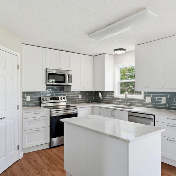 Modern white kitchen with stainless steel appliances and wooden floor.