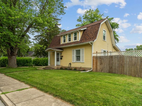 Yellow two-story house with brown roof and green lawn.
