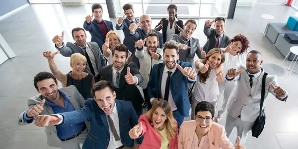 A diverse group of professionals giving thumbs up in an office setting.