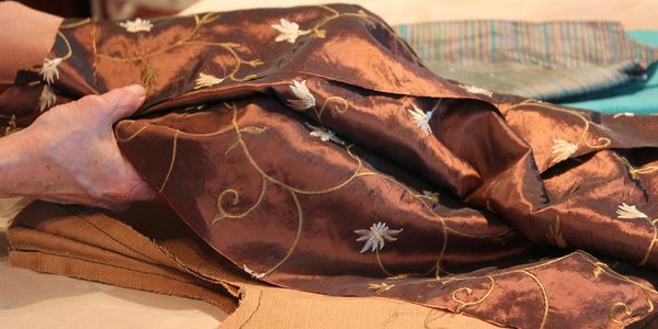 Hands holding embroidered brown fabric with floral patterns.