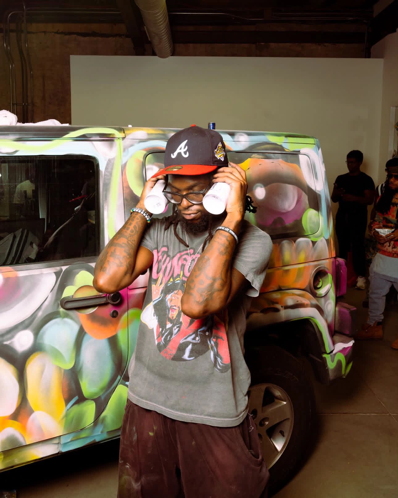 Man with painted van holding spray cans to his ears.