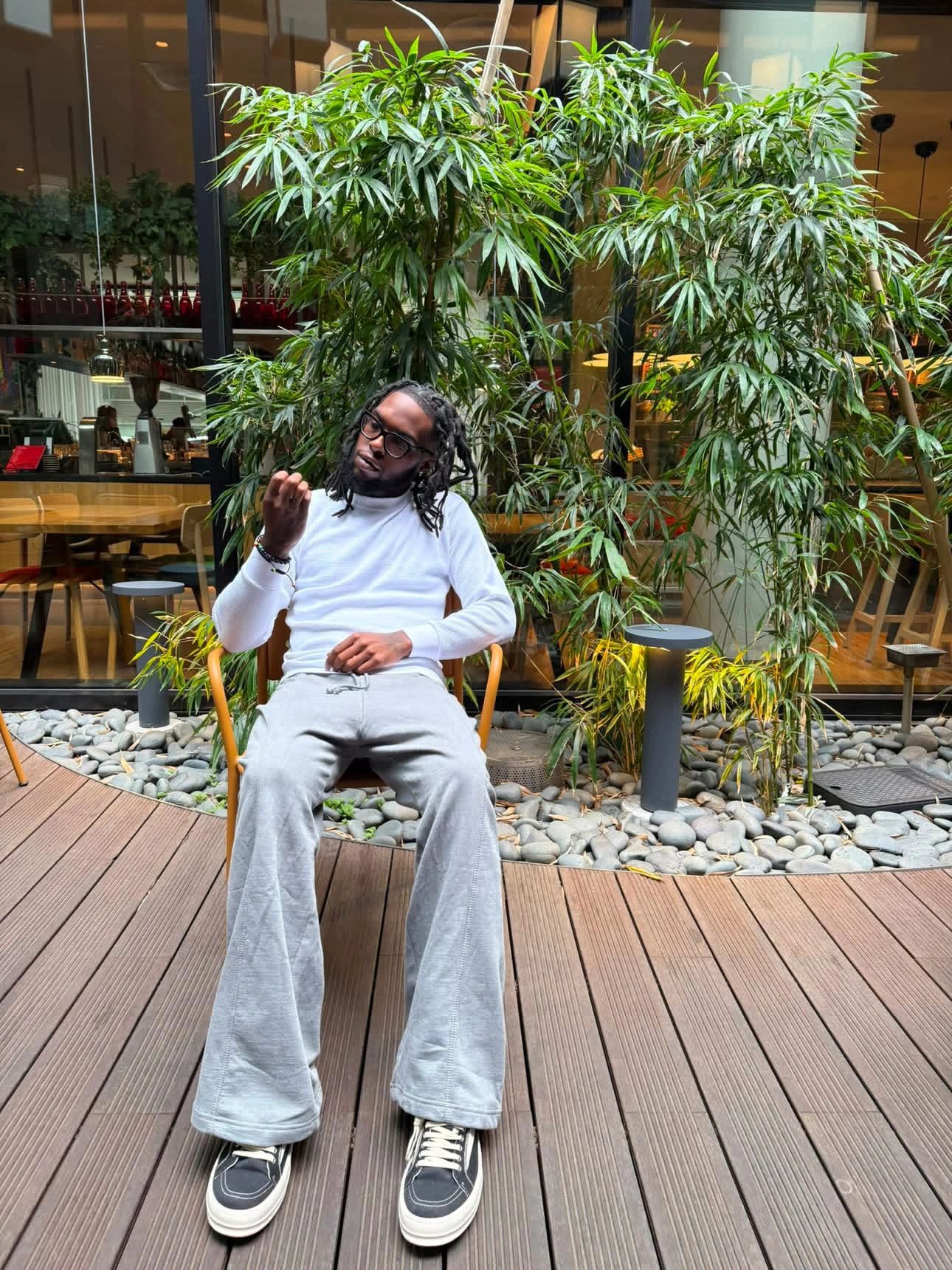 Man sitting on a chair in a relaxed pose with greenery behind him.