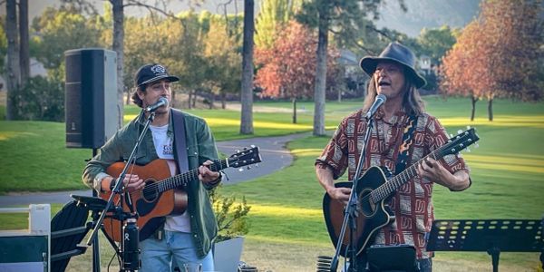 Two men playing guitars and singing outdoors.